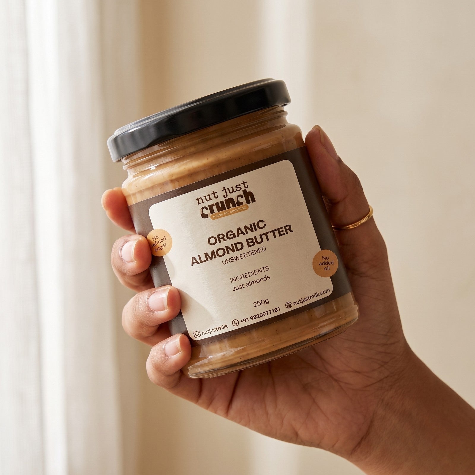 A hand holding the Nut Just Crunch Organic Almond Butter 250 g glass jar
